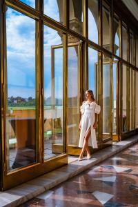 Una donna con un vestito bianco in piedi alla finestra di Grand Hotel International - Czech Leading Hotels a Praga