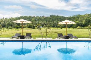 una piscina con sillas y sombrillas junto a un campo en The Bayou Hotel Langkawi, en Pantai Cenang