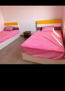 two beds in a bedroom with pink sheets and pillows at Amwaj north Coast 