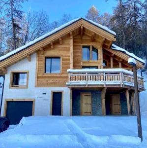 a log home with a deck on top in the snow at Chalet Kelly in Les Orres