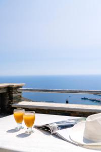 Dois copos de sumo de laranja numa mesa com o oceano. em Ktima Petrina Volia- Maisonette Phos em Andros
