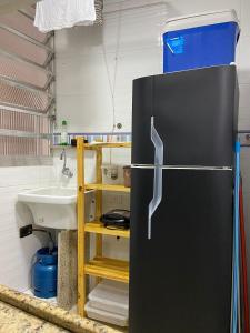 a black refrigerator in a kitchen with a sink at Estúdio charmoso um minuto a pé do mar in Guarujá