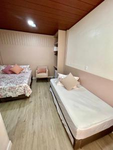 a room with two beds and a chair in it at Pousada Rota do Sol Quarto Filial Rose 11 in Penha