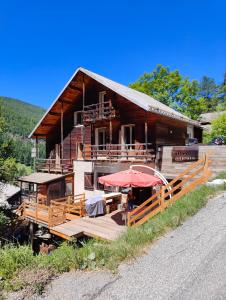 a large wooden house with a deck and umbrella at Chalet Ailleurs Appartement à Molines en Queyras in Molines-en-Queyras