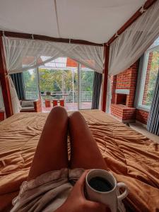 a person with their feet on a bed with a cup of coffee at Kubu Kawi in Munduk