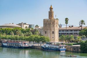 un grupo de barcos en un río con una torre en AlohaMundi Segovia&Fortaleza, en Sevilla