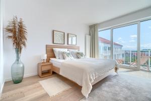 a white bedroom with a bed and a large window at Apartamenty Marina z widokiem na morze in Darłówko