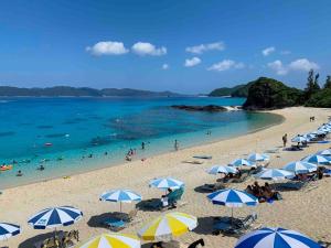 een strand met blauwe en witte parasols en mensen in het water bij HOMESTAY Kucha - Vacation STAY 17846v in Asa