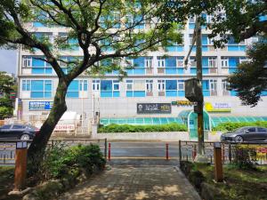 ein Gebäude mit einem Baum vor einer Straße in der Unterkunft Welcome to Jejubi house in Jeju-do