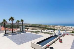 a swimming pool with palm trees and the ocean at Deluxe 2 Bedroom Flat - BeachFront - Praia Del Rey in Amoreira