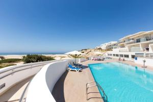 a swimming pool with chairs and the ocean in the background at Deluxe 2 Bedroom Flat - BeachFront - Praia Del Rey in Amoreira