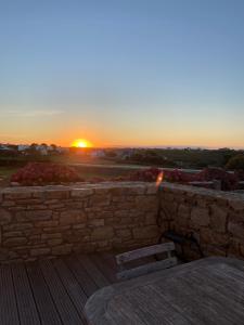 a sunset over a stone wall with a table and chairs at l'Aod, maison d'hôtes insulaire in Ouessant