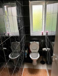 een zwart betegelde badkamer met een toilet en 2 ramen bij Whitechapel Rooms R3 in Londen
