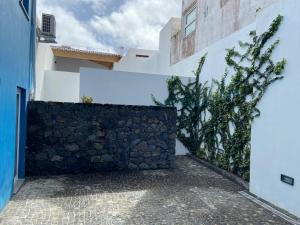 un muro di pietra accanto a un edificio bianco con un albero di A Casinha ad Angra do Heroísmo