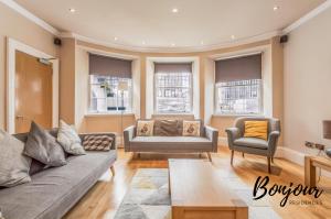 ein Wohnzimmer mit einem Sofa, 2 Stühlen und Fenstern in der Unterkunft Montmartre Suite - New Town 3BR-3BA Main Door - Free Parking & Patio by Bonjour Residences Edinburgh in Edinburgh