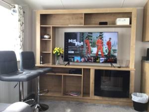 a entertainment center with a tv and two stools at Brookside West Sands Holiday Park Seal Bay Selsey in Selsey