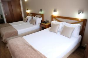 two beds in a hotel room with white pillows at Hotel Dona Sofia in Braga