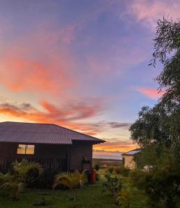 una casa en un campo con una puesta de sol en el fondo en Maunga Roa Eco Lodge en Hanga Roa