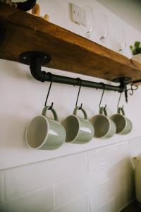 een rij koffiemokken hangend aan een plank bij Pebbles Cottage in Caister-on-Sea