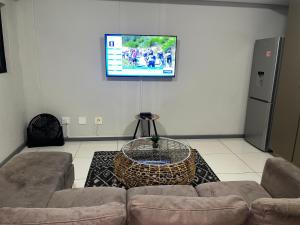 een woonkamer met een bank en een tv aan de muur bij The Den in Windhoek