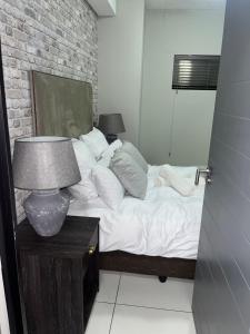 een slaapkamer met een bed met een lamp en een bakstenen muur bij The Den in Windhoek