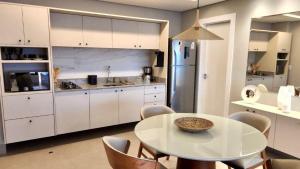 a white kitchen with a table and chairs and a refrigerator at Loft Ultra Luxo há Poucos Passos do Shopping CG. in Campo Grande