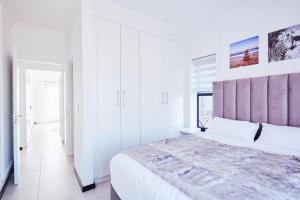 a white bedroom with a large bed with a purple headboard at Luxurious sandton apartment with Inverter in Sandton