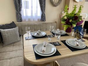 a dining room table with plates and wine glasses at Comfy Cosy Caravan_Romney Sands in Littlestone-on-Sea