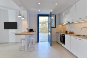 una cocina con armarios blancos y una mesa con taburetes en Villa & Studio Hydroussa by Andros Homes, en Gavrion