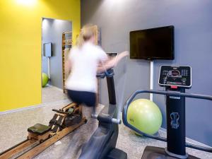 a woman riding an exercise bike in a gym at Aparthotel Adagio Köln City in Cologne