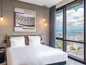 a bedroom with a white bed and a large window at Pullman Tbilisi Axis Towers in Tbilisi City