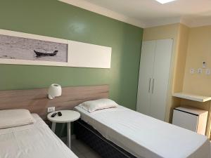 Habitación con 2 camas, mesa pequeña y lámpara. en Hotel Porto Grande en Maceió