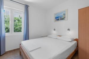 a white bedroom with a bed and two windows at Apartments by the sea Mandre, Pag - 6418 in Kolan