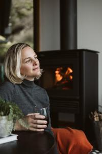 Eine Frau, die vor einem Kamin sitzt und ein Glas hält. in der Unterkunft Point of View Villas in Apollo Bay