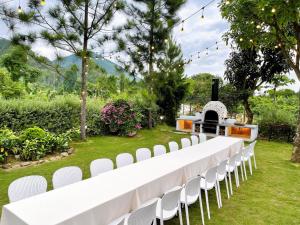 a long white table with white chairs in a garden at Nam Casa Sân Golf Tam Đảo Venuestay in Tam Ðảo