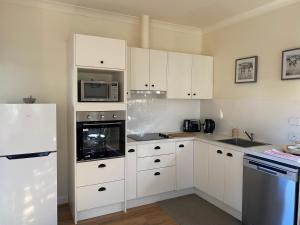 a kitchen with white cabinets and a refrigerator at King River Cottage in Moyhu