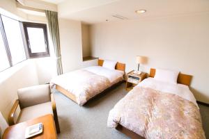 a bedroom with two beds and a chair and a window at Hotel Ohedo in Tokyo