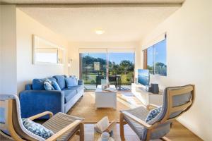 Una sala de estar con un sofá azul y sillas. en Intrepid, 15 3 Intrepid Close - right on the beachfront and WiFi, en Shoal Bay