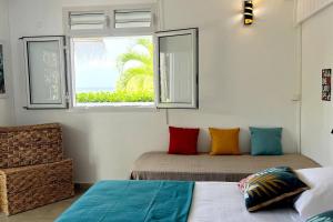 1 Schlafzimmer mit 2 Betten mit bunten Kissen und einem Fenster in der Unterkunft La Belle Vue - Grand studio vues mer et accès plages in Deshaies