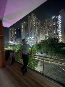 un uomo in piedi su un balcone in una città di notte di Luxurious 3 BHK Flat in Ghaziabad a Ghaziabad