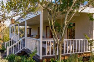 a white house with a porch and a tree at Valley Farm Stay in Knysna