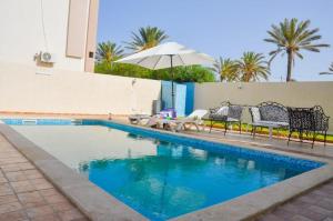 a swimming pool with two benches and an umbrella at MAISON RITEl 1 in Taguermess