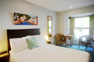 a bedroom with a white bed and a chair and windows at Penryn House Hotel in Polperro