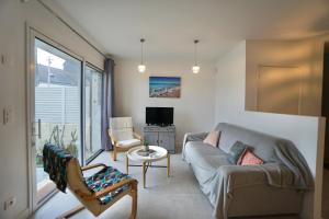 ein Wohnzimmer mit einem Sofa, Stühlen und einem TV in der Unterkunft Le Clos de l'Anse *front de mer* in Ploemeur