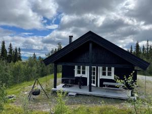 ein kleines schwarzes Haus mit einer Veranda und einer Bank in der Unterkunft Linnaeus - 6 person cabin in Ål