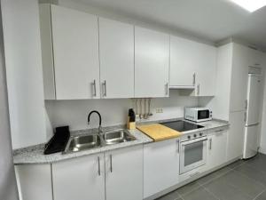 a white kitchen with a sink and a refrigerator at Apartamento en palmeira - Colores del Barbanza Naranja in Ribeira