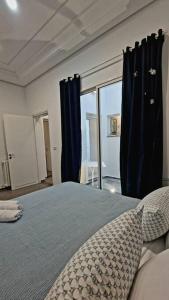1 dormitorio con 1 cama con cortinas azules y ventana en La Maisonnette Turquoise, en Dar Mimoun Bey