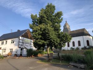 a white building with a tree and a church at Waldmomente in Schauren