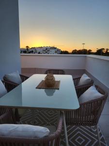 ÁTICOS ROTA Punta Candor في روتا: طاولة بيضاء وكراسي على شرفة مع غروب الشمس