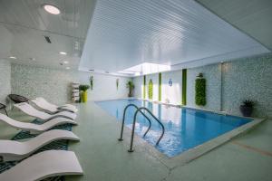 a swimming pool with white chairs in a building at Hôtel et SPA du Château in Lagord